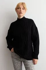 Polerón de punto negro con cuello alto y diseño de trenzas verticales en el frente. Posee mangas largas con puños acanalados y un corte holgado.