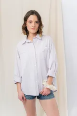 Camisa verde pastel de algodón, corte oversize, con cuello camisero, cierre con botones, mangas largas con puños con volados de encaje blanco, dos bolsillos frontales con solapa y ruedo irregular. 