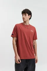 Remera de manga corta color terracota con estampado frontal blanco que dice "MISTRAL Architecture of Reality REG. TM / EST. 76". Tiene un fit regular y está confeccionada en algodón.