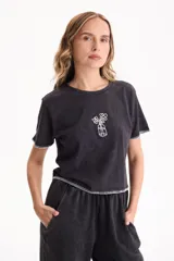 Remera crop negra con efecto acid wash, mangas cortas con costuras decorativas en blanco y bordado frontal de un florero con flores.