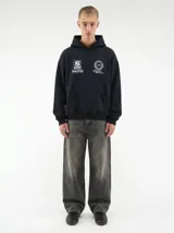 Hoodie negro con capucha, diseño estampado en la espalda con el logo de la marca dentro de un círculo de laureles y texto en la parte posterior de la capucha.