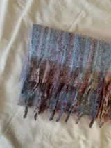 Bufanda de tejido de punto suave y esponjoso con diseño de rayas verticales en tonos azulados, marrones y toques de colores vibrantes, terminada con flecos largos en los extremos.