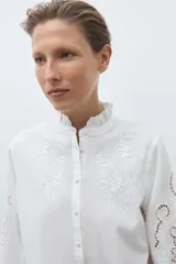 Camisa blanca de manga larga con cuello alto fruncido y bordados calados en el pecho y los hombros.