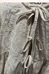 Blusa beige de lino bordado, calce holgado, escote en V con doble lazo ajustable y mangas 3/4 con volumen.