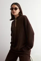 Sweater de tejido acanalado color marrón, con cuello alto y cierre frontal parcial. Presenta un diseño holgado de manga larga con hombros caídos.