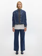 Campera de denim azul oscuro con cuello redondo, cierre frontal con botones metálicos y tachas plateadas en el frente y la espalda.