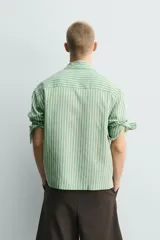 Camisa de corte relajado confeccionada en tejido fluido con mezcla de lyocell. Presenta diseño de rayas verticales, cuello solapa, manga larga con puños abotonados, bolsillos de plastrón con solapa en el pecho y cierre frontal con botones a presión.