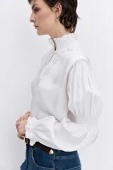 Blusa celeste de manga larga con puños fruncidos y elásticos, escote en V con cuello alto con volados y delicados bordados florales en el pecho.