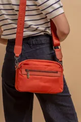 Bandolera de diseño moderno y funcional, confeccionada en nylon color marrón claro. Cuenta con múltiples compartimentos con cierre metálico, herrajes plateados y una correa ancha ajustable con detalle de marca.