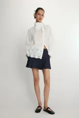 Camisa de manga larga en color blanco, confeccionada con detalles de bordados perforados a tono. Presenta un cuello tipo pañuelo y cierre frontal con botones.