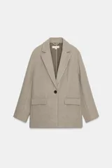 Blazer de corte recto y diseño minimalista, confeccionado en tejido de paño suave color beige. Presenta cuello con solapas clásicas, cierre frontal con un solo botón y dos bolsillos delanteros con solapa.