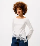 Blusa de algodón con cuello bote y mangas largas. Presenta un diseño asimétrico en el bajo decorado con un delicado detalle de encaje.