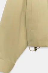 Cazadora bomber de color beige con cuello subido, manga larga y bolsillos delanteros. Cuenta con cierre frontal de cremallera metálica y cordón ajustable en el dobladillo.