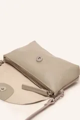 Cartera bandolera color beige, confeccionada en 100% cuero, con solapa redondeada, detalle de flor grabada y correa larga ajustable.