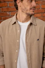 Camisa de pana color beige, de corte slim fit, con cuello clásico y cierre frontal de botones. Cuenta con un pequeño bordado de ave en el pecho.