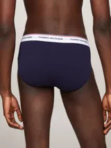 Pack de tres calzoncillos tipo slip de la marca Tommy Hilfiger, confeccionados en algodón elástico, con cintura elástica con el nombre de la marca y líneas distintivas. Incluye una unidad con cintura blanca, otra con cintura azul marino y otra con cintura roja.