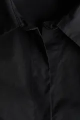 Camisa entallada negra de tejido elástico, con cuello abierto y cierre frontal de botones. Cuenta con mangas largas con puños anchos abotonados, además de pinzas delanteras y traseras para estilizar la figura.
