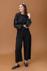 Sweater negro de cuello redondo con mangas largas decoradas con lentejuelas brillantes del mismo tono. Presenta puños y ruedo acanalados, con un corte relajado y cómodo.