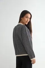 Buzo de punto con diseño a rayas horizontales finas, cuello redondo y puños en color negro. Presenta un corte holgado y mangas largas.