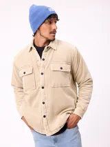 Sobrecamisa de pana color beige, con cierre frontal de botones a presión, dos bolsillos frontales con solapa y bolsillos laterales. Presenta cuello clásico y diseño acolchado con forro interior.