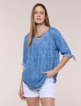 Blusa azul de lyocell con estampado floral, escote en V con bordado y aplique de cuentas de madera, mangas tres cuartos con lazos ajustables en los puños y diseño holgado.