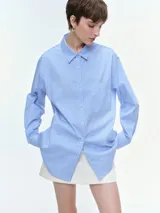 Camisa oversize de popelina de algodón con diseño de rayas verticales, cuello clásico, cierre frontal con botones, manga larga con puños anchos y bolsillo aplicado en el pecho.