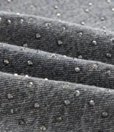 Pantalón de jean de corte recto y tiro medio, color gris con acabado lavado y aplicaciones de brillos distribuidas en las piernas. Cuenta con diseño de cinco bolsillos, cierre frontal con botón y costuras reforzadas.