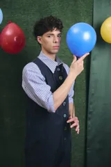 Mono largo de color negro con cierre frontal de botones vintage de distintos colores. Presenta un diseño sin mangas, con bolsillos laterales y una cinta para herramientas en la parte trasera.