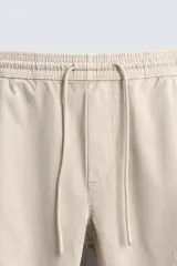 Pantalón tipo jogger de corte slim fit, confeccionado en tejido de algodón con elasticidad. Presenta cintura elástica ajustable con cordón, bolsillos frontales, bolsillos traseros de vivo y bajos con puños elásticos.
