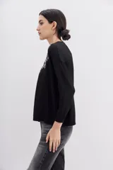 Sweater negro de manga larga y calce holgado, con terminaciones en punto rib. Presenta un bordado frontal con la frase "Tonight the night" realizado con canutillos y piedras de colores.