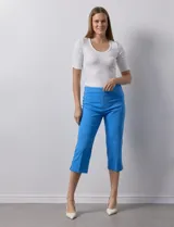 Pantalón capri blanco de gabardina elastizada. Pretina ancha elastizada, delantera con bolsillos simulados y trasera con bolsillos aplicados.