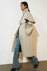 Gabardina larga de corte recto y diseño minimalista en color beige, con cuello solapa, manga larga y cierre frontal con botones. Cuenta con una capa desmontable en el mismo tejido y una solapa decorativa en el pecho.