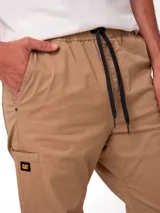 Pantalon de corte utilitario color tostado, con cintura elástica y cordón de ajuste. Presenta bolsillos laterales, un bolsillo utilitario en la pierna derecha con etiqueta de la marca y remaches metálicos en los bolsillos.