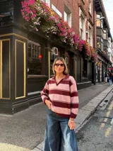 Sweater tejido de punto con diseño de rayas horizontales anchas en tonos rosado y bordó, corte holgado, mangas largas y cuello tipo polo con escote en V.