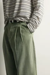 Pantalón chino baggy fit color verde militar, confeccionado en denim de algodón rígido, con corte holgado, tiro medio y pliegues frontales. Presenta bolsillos laterales y cierre frontal con cremallera y botón, con efecto lavado.