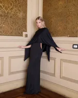 Capa de diseño elegante en color negro, confeccionada en tejido fluido con caída suave. Presenta un corte amplio que cubre los hombros y brazos, ideal para complementar vestidos de fiesta.