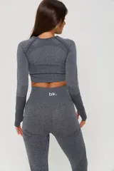 Conjunto deportivo de dos piezas compuesto por un top de manga larga tipo crop top con aberturas para pulgares y una calza de tiro alto. Ambas prendas presentan un diseño seamless con detalles de texturas perforadas y el logo de la marca estampado en el frente.