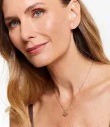 Conjunto de collar y caravanas doradas. El collar es de cadena fina con colgante circular con diseño de árbol de la vida calado. Las caravanas son aros pequeños con un punto de luz.