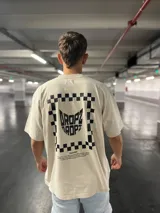 Remera de algodón con efecto acid wash color verde oliva, corte relajado y manga corta. Estampa grande en la espalda con marco de damero y logo 'Dropz' en el centro, junto a un texto motivacional bajo el título 'Panther'.