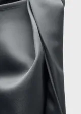 Vestido corto de tejido satinado fluido con diseño recto, cuello redondo y detalle de nudo en el hombro. Es una prenda sin mangas de estilo minimalista.