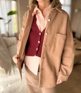 Sobre camisa oversize de paño color camel, con cuello camisero, cierre frontal de botones metálicos y bolsillos frontales tipo parche.