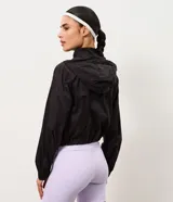 Campera rompevientos marrón de corte cropped, con capucha, cierre frontal de cremallera, cuello alto y puños elásticos.