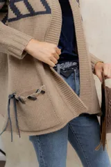 Saco tejido de punto con diseño de guarda inca en la parte superior. Presenta bolsillos frontales con detalles de tiras de cuero y flecos. De corte recto y largo medio, con terminaciones en tejido acanalado.