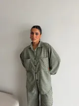 Camisa de viyela con estampado de cuadros en tonos marrones, beige y negro. Presenta cuello clásico, cierre frontal con botones, mangas largas con puños abotonados y dos bolsillos delanteros con solapa.