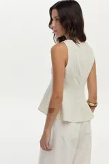 Top de lino color beige con cuello bote y diseño con peplum, sin mangas y con cierre invisible en la espalda.
