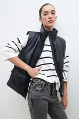 Chaleco negro de cuero sintético con cuello alto, cierre frontal con cremallera y bolsillos laterales con solapa.
