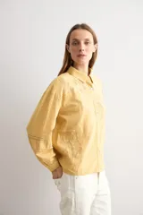 Camisa amarilla de manga larga con detalles bordados y calados en los hombros, pecho y mangas, corte clásico con cuello camisero y cierre frontal de botones.