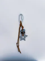 Charm para bolso o accesorios con mosquetón metálico, tejido de macramé en cordón negro y dijes de cerámica esmaltada en tonos violeta y celeste.