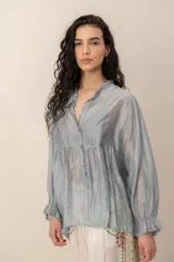 Blusa de seda gris con mangas largas abullonadas y puños con volados, escote en V con cuello fruncido y botones frontales.
