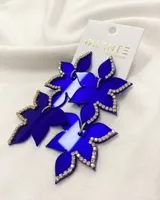 Par de aros colgantes con forma de flor de acrílico color azul eléctrico, con borde de strass plateado y gancho dorado.